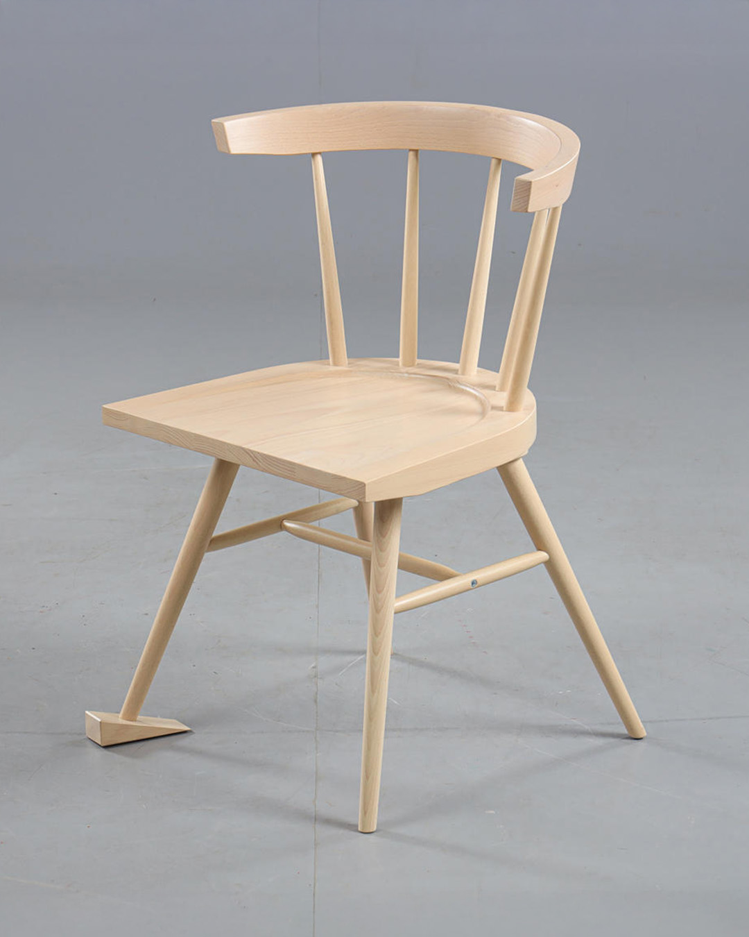 Virgil Abloh x IKEA chair with a curved back, pale wood finish, and intentionally uneven legs, photographed against a gray studio background.